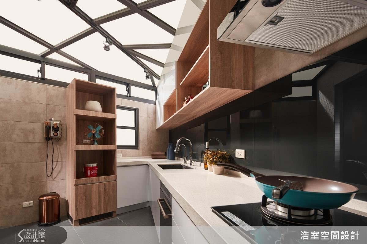 將廚房移住後院，加高圍牆高度後再加氣窗，就成為隱蔽的私人空間，上方天花板是透光性強的採光罩，配合地形做出倒勾狀的流理台，在廚房空間裡一點兒也不奇怪，反而符合料理動線。鐵灰色的烤漆玻璃呼應上方不規則金屬支架的深色，穩住空間氛圍。