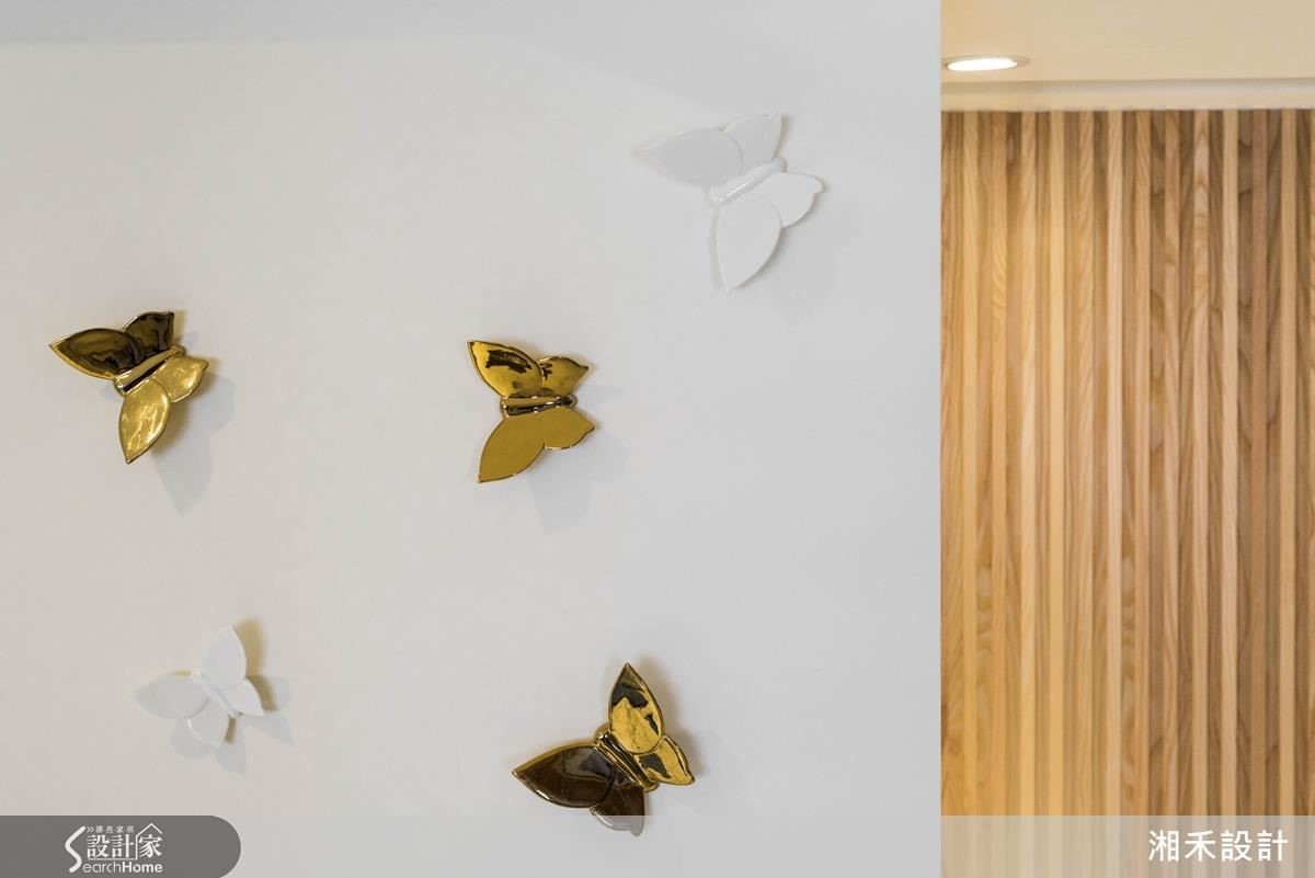 客廳的白色立面上，陶藝品蝴蝶既是與女屋主優雅氣質相符的裝飾品，也是櫃體的把手；金色的質感與木作線條牆面互相呼應，這些巧思串起空間中豐富色彩與質感的整體性。