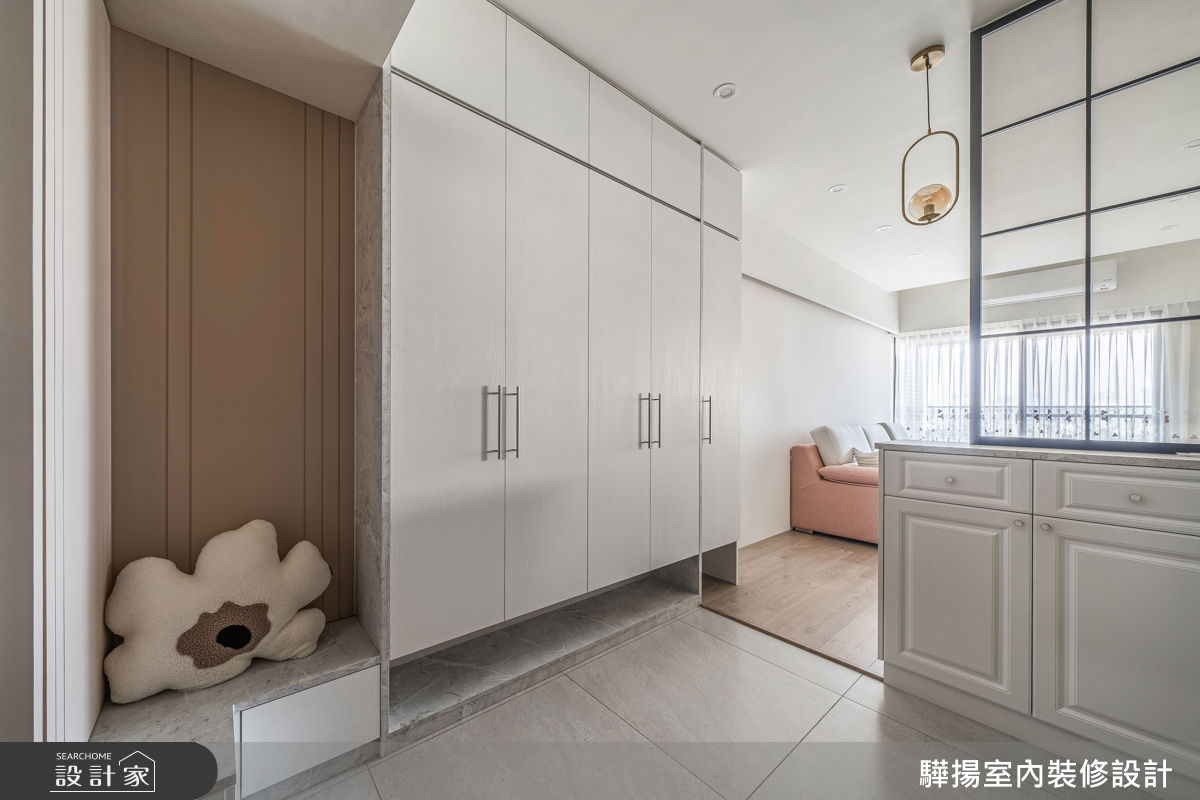 玄關設有體貼長輩的穿鞋椅，並結合白色收納櫃及鐵件玻璃屏風，化解穿堂煞，且維持光線穿透。