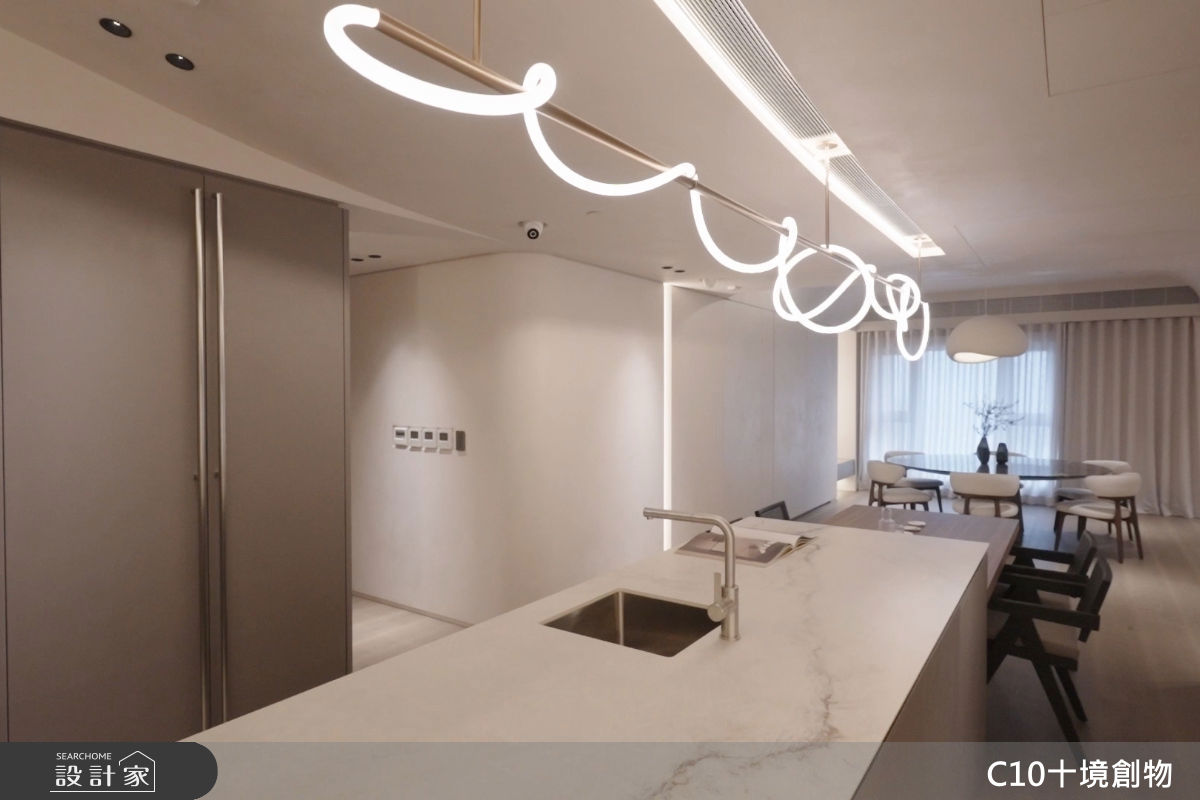 中島和餐桌上方的弧形燈帶不僅延伸視覺尺度，也讓空間的光影更立體。