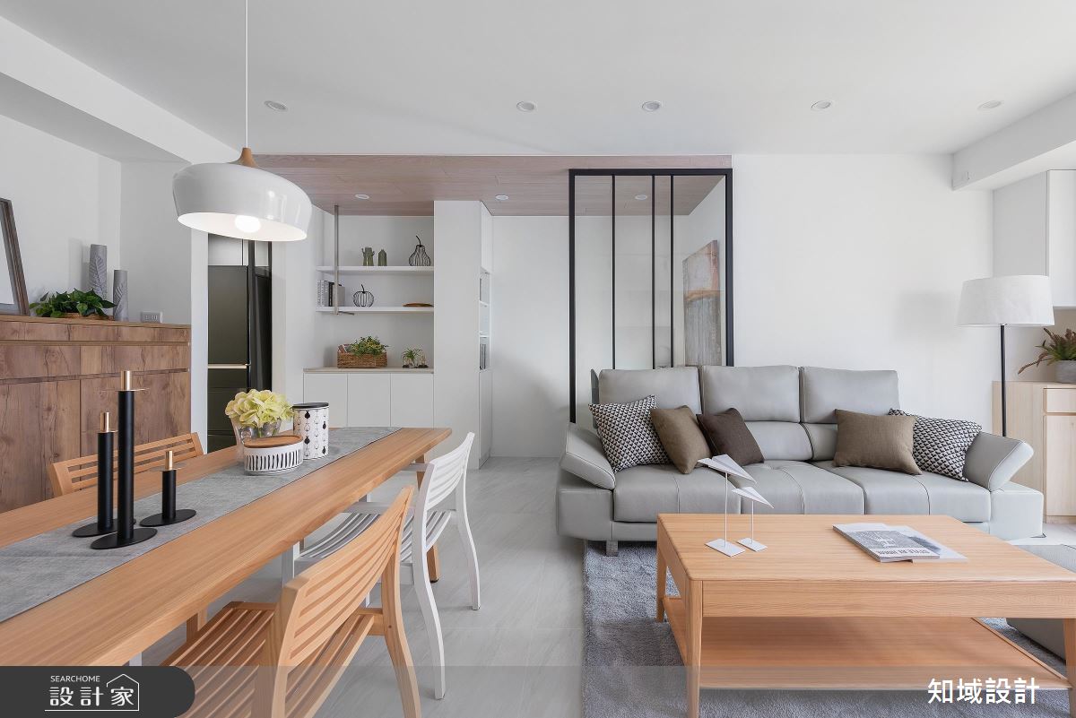 簡單的玻璃鐵件屏風，區隔出客廳與玄關的空間，空間整體灰白黑的配色略微冷調，使用木質家具在空間裡注入了溫潤的氛圍。